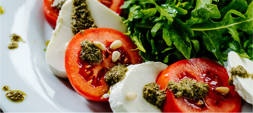 Mozzarella and tomato salad with arugula and pesto drizzled on top.